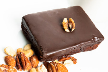 Shallow focus view of delicious chocolate fudge brownie and walnut garnish on top; on white platter with mixed nuts