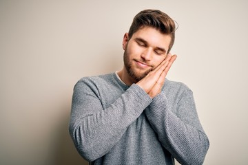 Young handsome blond man with beard and blue eyes wearing casual sweater sleeping tired dreaming and posing with hands together while smiling with closed eyes.