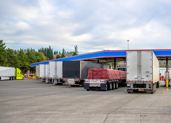 Different big rigs semi trucks with loaded semi trailers standing on the fuel station for refueling...