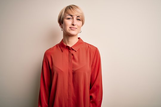 Young beautiful business blonde woman with short hair standing over isolated background Relaxed with serious expression on face. Simple and natural looking at the camera.
