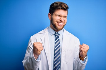 Young blond therapist man with beard and blue eyes wearing coat and tie over background very happy and excited doing winner gesture with arms raised, smiling and screaming for success. Celebration 