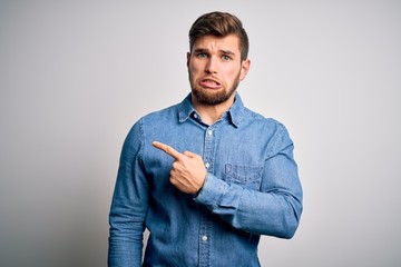 Young handsome blond man with beard and blue eyes wearing casual denim shirt Pointing aside worried and nervous with forefinger, concerned and surprised expression