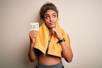 Young african american sportswoman wearing towel holding reminder with diet message serious face...