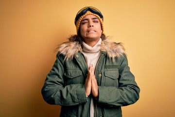 Young african american afro skier girl wearing snow sportswear and ski goggles begging and praying with hands together with hope expression on face very emotional and worried. Begging.