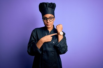 Young african american chef girl wearing cooker uniform and hat over purple background In hurry pointing to watch time, impatience, looking at the camera with relaxed expression