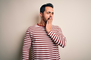 Fototapeta premium Young handsome man with beard wearing casual striped t-shirt standing over white background bored yawning tired covering mouth with hand. Restless and sleepiness.