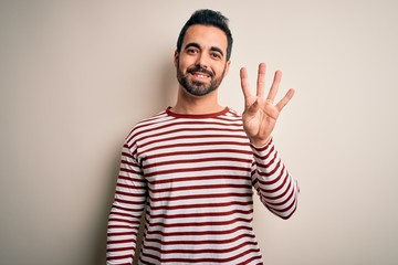 Naklejka premium Young handsome man with beard wearing casual striped t-shirt standing over white background showing and pointing up with fingers number four while smiling confident and happy.