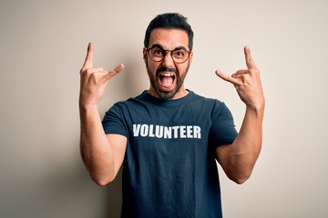 Handsome man with beard wearing t-shirt with volunteer message over white background shouting with...