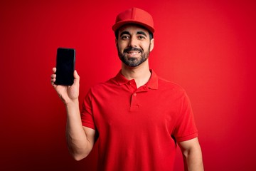 Young handsome delivery man with beard holding smartphone showing deliver food app with a happy face standing and smiling with a confident smile showing teeth