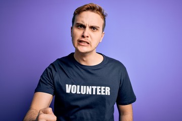 Young handsome redhead man wearing volunteer t-shirt over isolated purple background annoyed and...