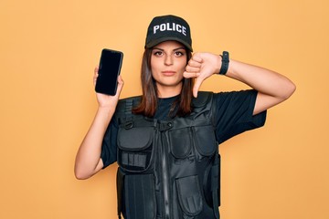 Beautiful brunette policewoman wearing police uniform holding smartphone showing screen with angry...