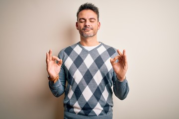 Fototapeta premium Young handsome man wearing casual sweater standing over isolated white background relax and smiling with eyes closed doing meditation gesture with fingers. Yoga concept.