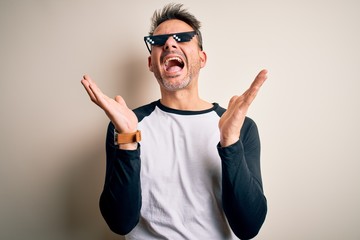 Naklejka premium Young handsome man wearing funny thug life sunglasses meme over white background celebrating mad and crazy for success with arms raised and closed eyes screaming excited. Winner concept
