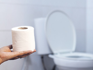 hand holding tissue over blurry white toilet background.