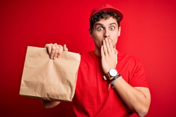 Young blond delivery man with curly hair wearing cap holding paper bag with food cover mouth with hand shocked with shame for mistake, expression of fear, scared in silence, secret concept