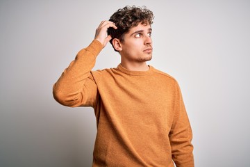 Young blond handsome man with curly hair wearing casual sweater over white background confuse and...