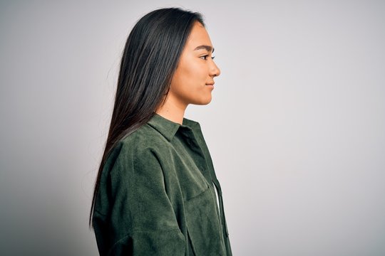 Young Beautiful Asian Woman Wearing Casual Shirt Standing Over Isolated White Background Looking To Side, Relax Profile Pose With Natural Face With Confident Smile.