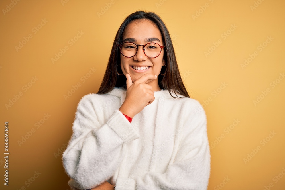 Wall mural young beautiful asian woman wearing casual sweater and glasses over yellow background looking confid