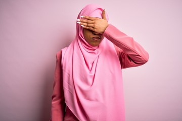 Young African American afro woman wearing muslim hijab over isolated pink background covering eyes with hand, looking serious and sad. Sightless, hiding and rejection concept