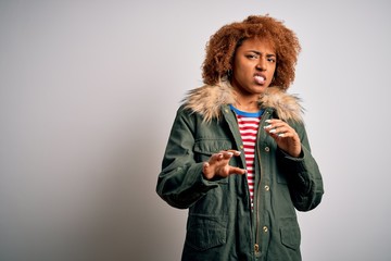 Young beautiful African American woman with curly hair wearing green casual winter coat disgusted expression, displeased and fearful doing disgust face because aversion reaction. With hands raised