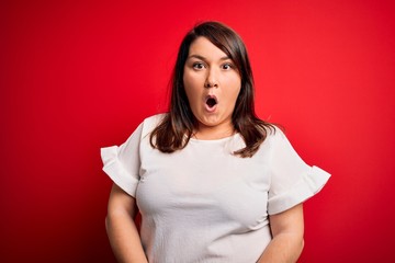 Beautiful brunette plus size woman wearing casual t-shirt over isolated red background afraid and shocked with surprise expression, fear and excited face.