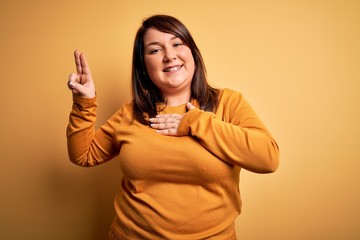 Beautiful brunette plus size woman wearing casual sweater over isolated yellow background smiling...