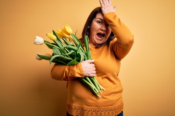 Beautiful plus size woman holding romantic bouquet of natural tulips flowers over yellow background...