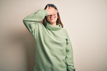 Young beautiful woman wearing casual sweater standing over isolated white background smiling and laughing with hand on face covering eyes for surprise. Blind concept.