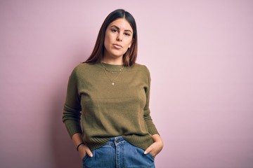 Young beautiful woman wearing casual sweater standing over isolated pink background with serious expression on face. Simple and natural looking at the camera.