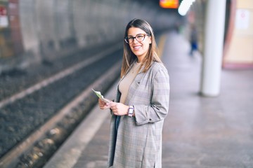 Young beautiful woman smiling happy and confident. Standing with smile on face  holding tickets at platform of train station