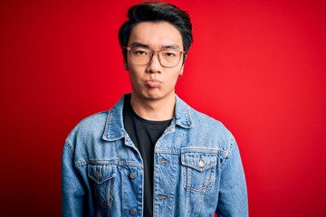 Fototapeta premium Young handsome chinese man wearing denim jacket and glasses over red background depressed and worry for distress, crying angry and afraid. Sad expression.