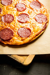 Fresh pepperoni pizza served on the wooden board. Selective focus. Shallow depth of field.