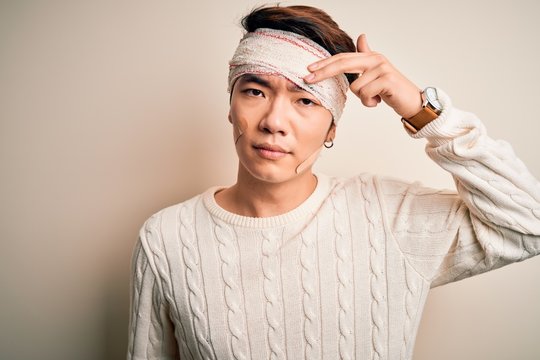 Young handsome chinese man injured for accident wearing bandage and strips on head pointing unhappy to pimple on forehead, ugly infection of blackhead. Acne and skin problem