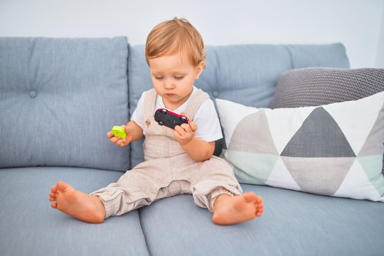 Adorable blonde toddler sitting on the sofa playing at home