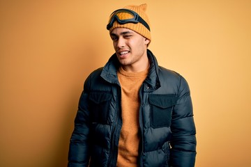 Young brazilian skier man wearing snow sportswear and ski goggles over yellow background winking looking at the camera with sexy expression, cheerful and happy face.