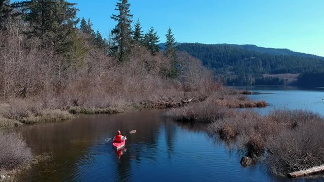 Man padding a kayak on Canadian lake with mountains in background and birds flying.