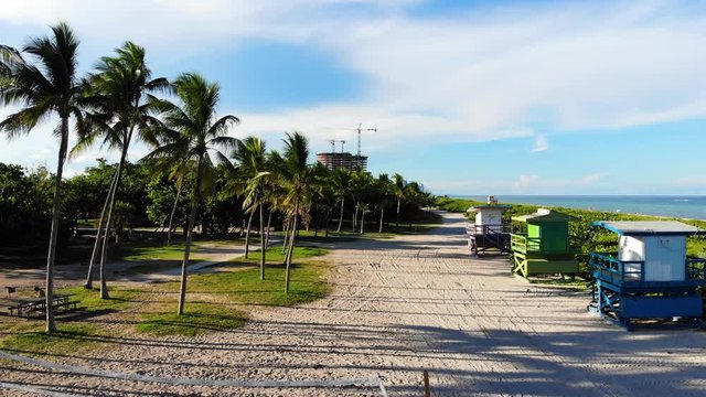 Moving along sandy path by the beach with lifeguard towers in storage and palms trees swaying gentle in the breeze.