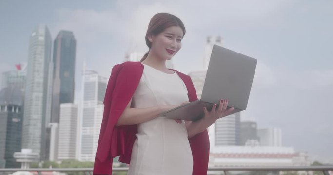 Successful and Confident Asian Chinese businesswoman wearing a red and white suit working in her laptop in Singapore business district