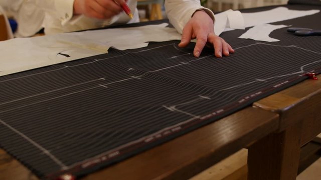 Hands of male tailor drawing pattern in studio. man's hand draws with chalk geometry on wool fabric. This Designer for clothes and tailor artist working for traditional fashion