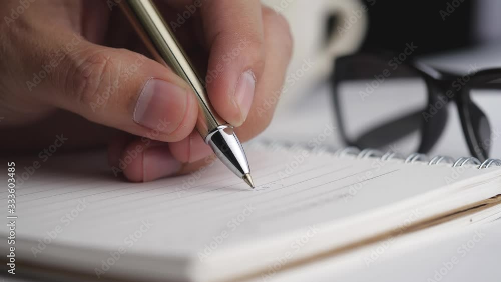 Poster close-up of male hands writing in spiral notepad placed on white desktop with various items