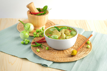 Thai food chicken green curry on wooden plate ,sliced chicken beast fillets, quartered eggplants, pea eggplant, basil leaves , pepper and coconut milk. green curry paste.