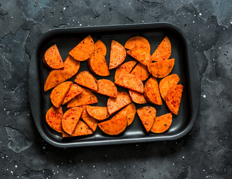 Raw sweet potato slices on a baking tray on a dark background, top view. Cooking baked sweet potatoes