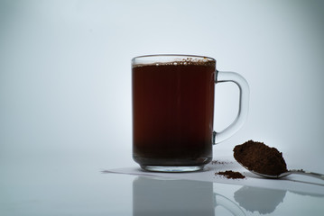 transparent cup with natural coffee and a spoon of ground coffee with star anise on a light background
