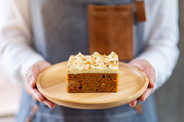 A waitress holding and serving a piece of homemade carrot cake in wooden tray