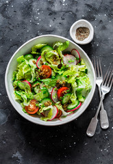 Easy vegetarian vegetable salad with fresh vegetables. Cherry tomatoes , romano lettuce, cucumbers, radishes and french mustard, olive oil, lemon salad dressing on a dark background, top view