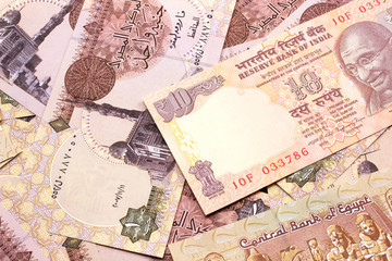 A close up image, shot in macro, of an orange, ten rupee Indian bank note on a bed of brown, one Egyptian pound notes