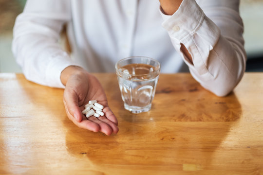 Closeup image of a woman holding white pills and a glass of water