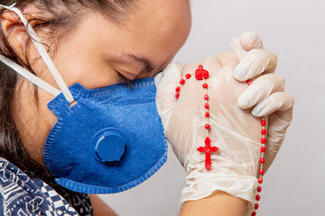 white woman praying wearing blue mask with a third in her hands, protection against coronavirus.