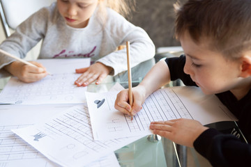 Schoolboy and schoolgirl writing letters. Close-up  pencil in the hand of child. Children learning to write letters at the table. A home distance learning.