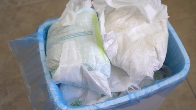 Smelling dirty disposable diapers in a garbage paill. Disposing of used baby nappies. Bathroom waste